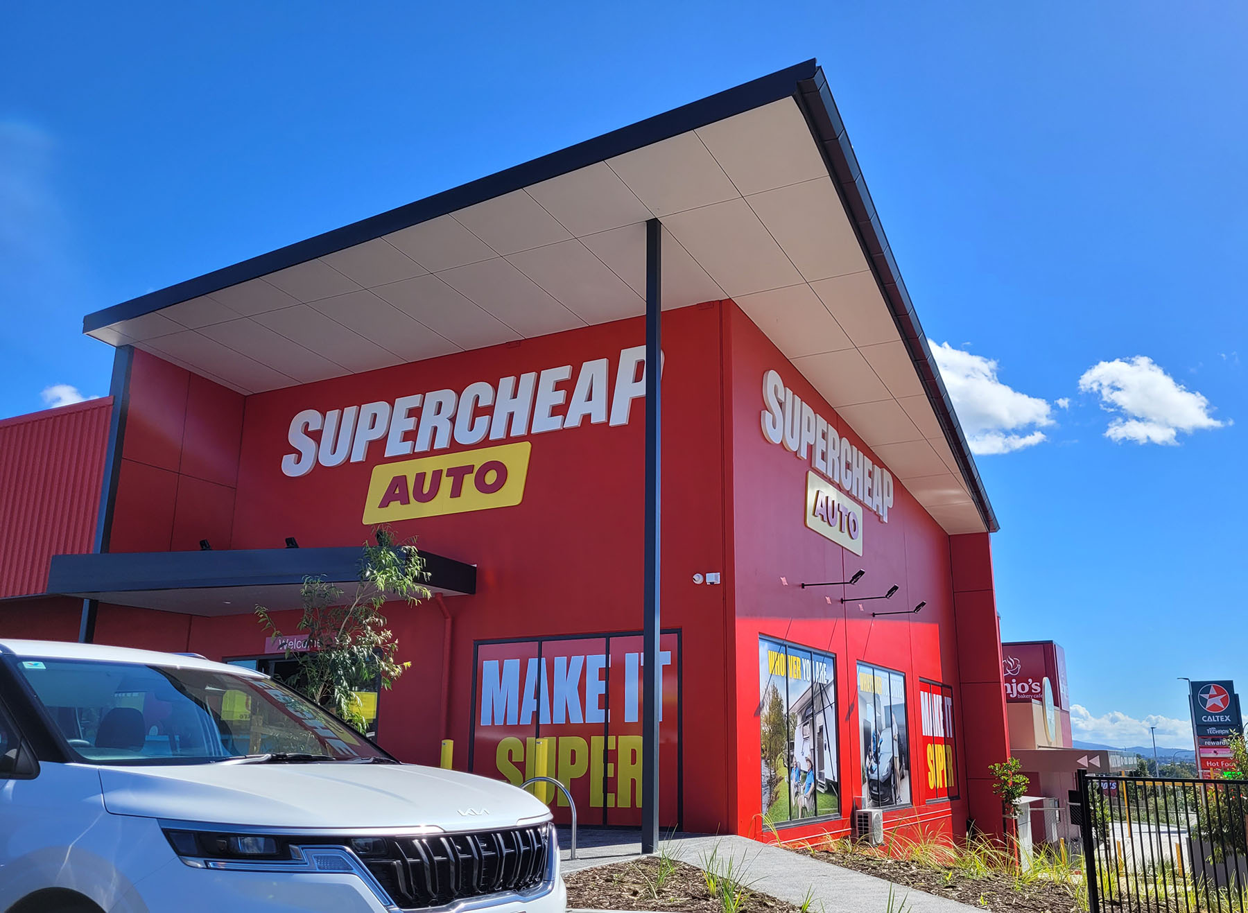 Exterior view of industrial and warehouse-style retail buildings, featuring prominent advertising and Supercheap Auto branding in red and yellow tones.