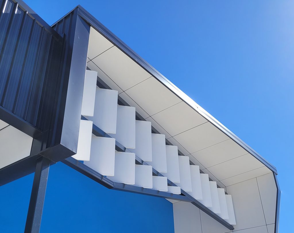 Close-up view of an aluminium exterior façade in blue, white and black, showcasing a fixed shutter-like system.