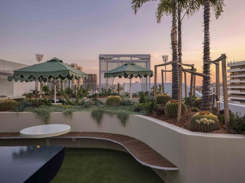 This image is taken on the roof of story house, it displays the garden bed, outdoor curved seating and green umbrellas.
