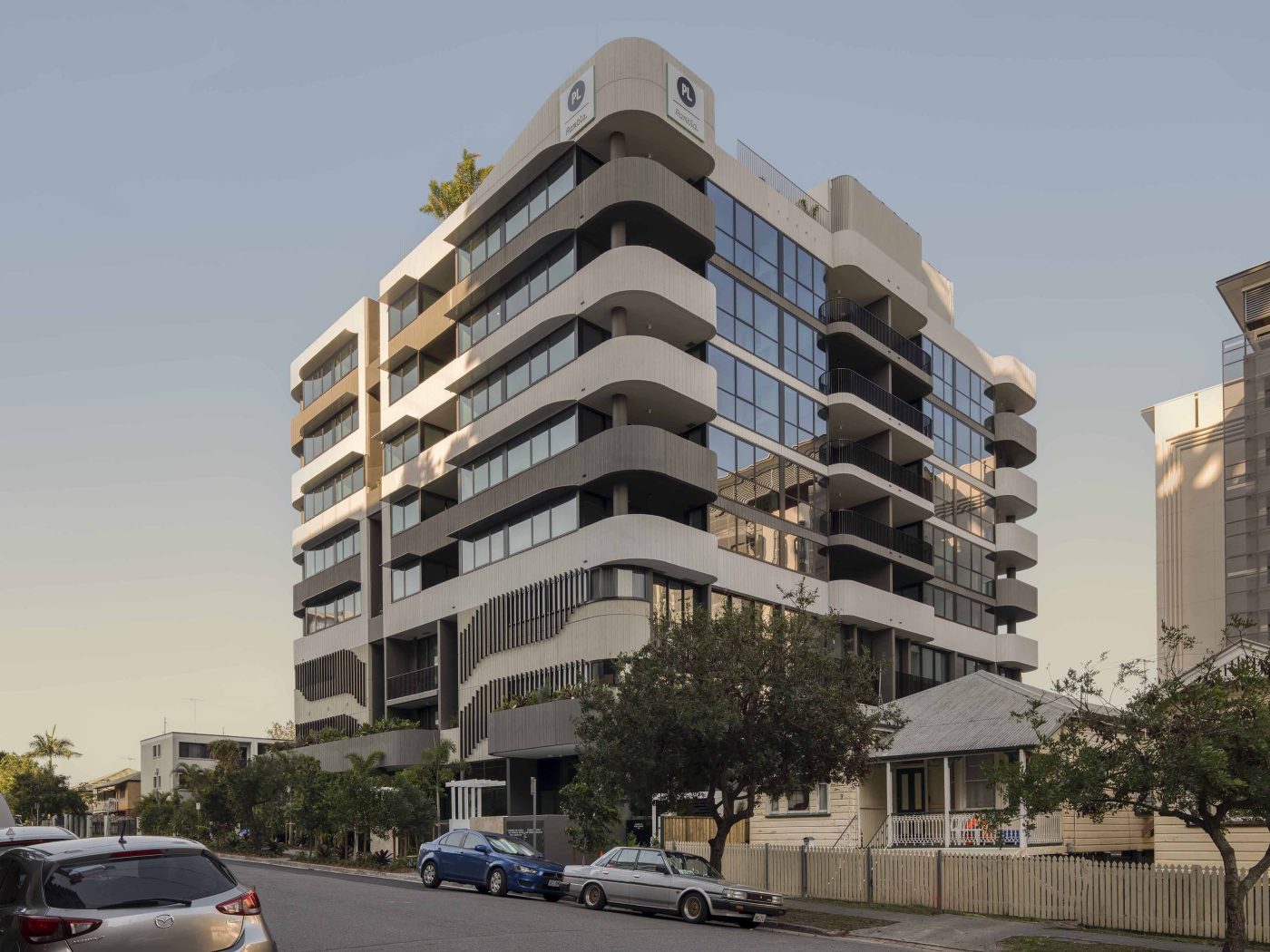 Exterior, multi-residential building, 8 storeys, white and grey building, trees and scrubs at the bottom.