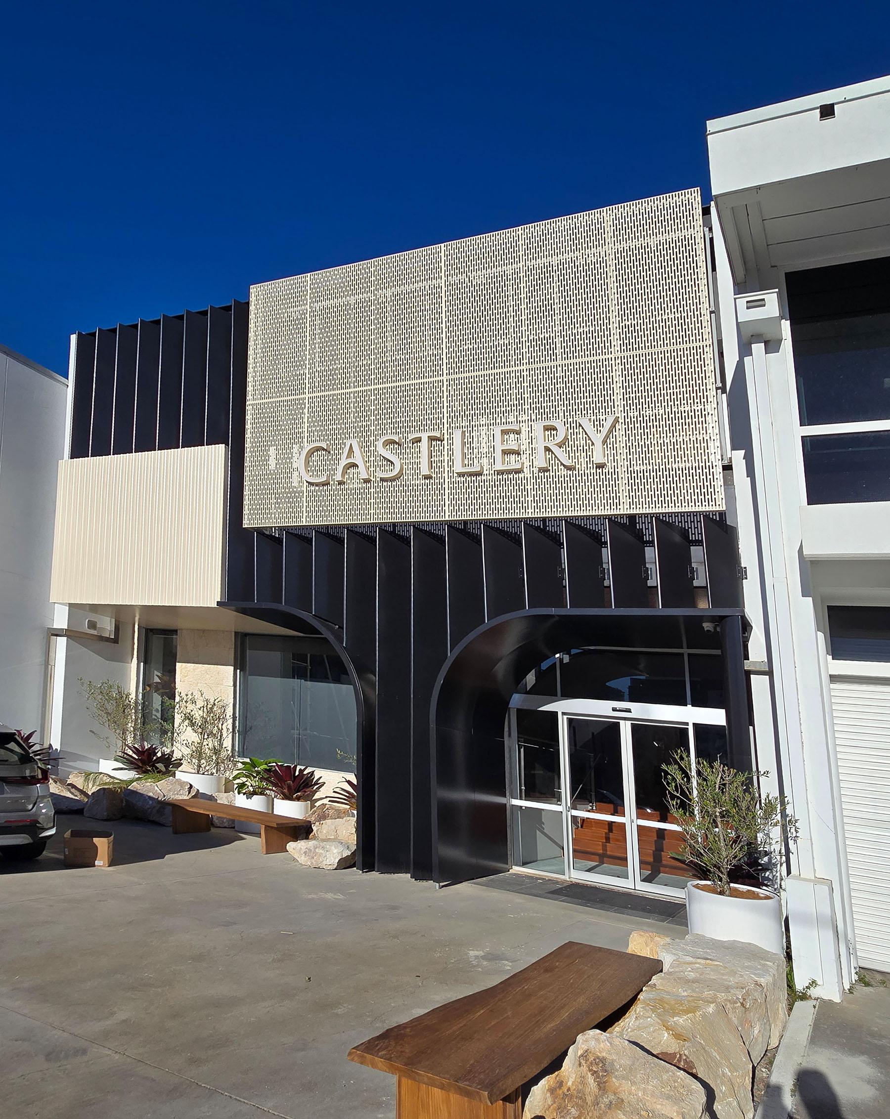 Castlery metal facade displaying black and cream colours, seating areas and large rocks.